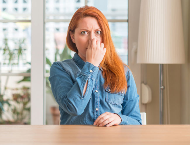 A woman with red hair covering her nose and holding her breath