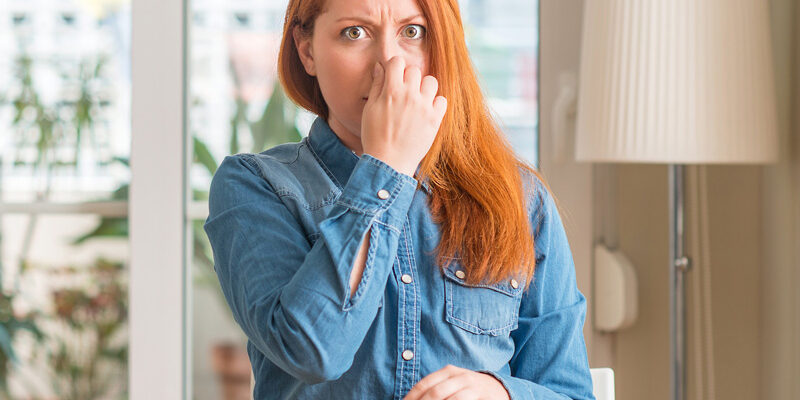 A woman with red hair covering her nose and holding her breath