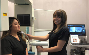 A woman sitting in a CT imaging machine and a woman operating the machine