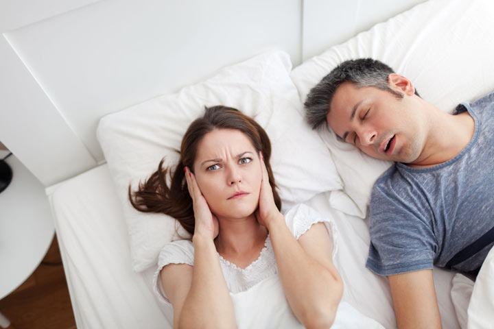 Woman plugging her ears next to a snoring man