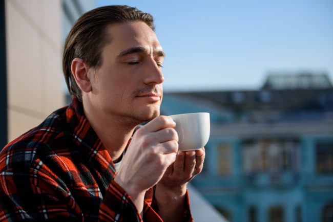 A man standing outside as he smells his cup of coffee