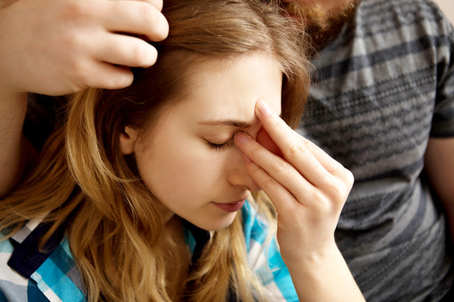 Young woman sitting on sofa with sinus pain, her partner is carring on her.