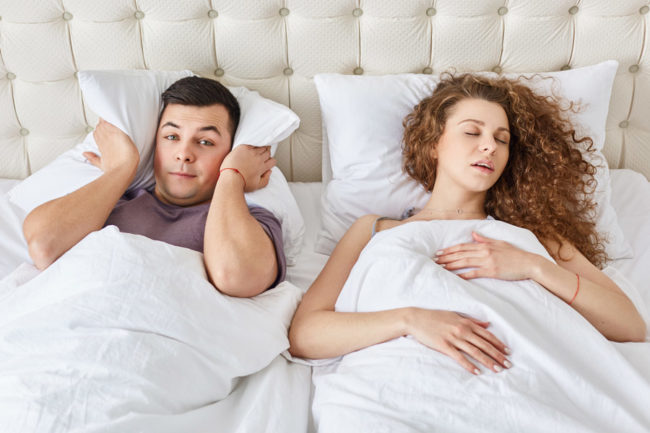 Man covers his ears as the woman next to him snores