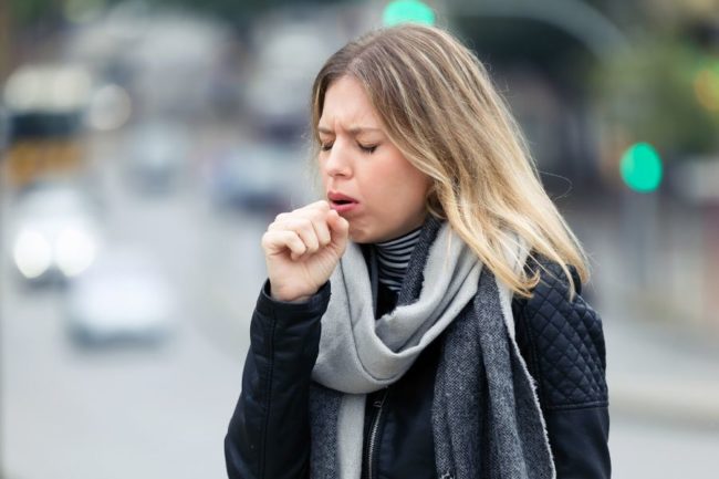 Woman coughing due to post nasal drip wearing a scarf and a black jacket