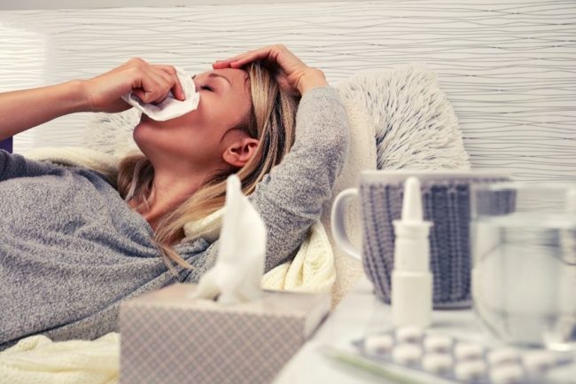 Woman suffering from sinus congestions and blowing her nose with medicine and water next to her