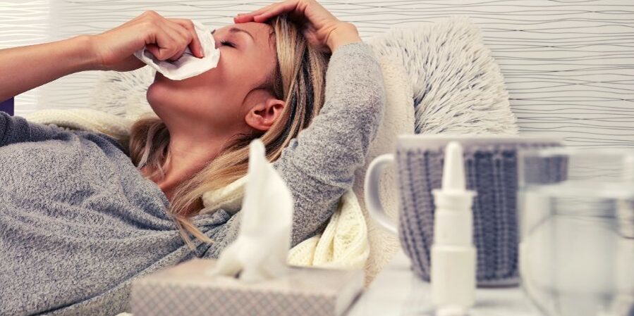 Woman suffering from sinus congestions and blowing her nose with medicine and water next to her